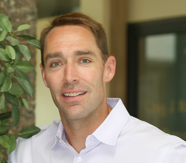 photo of Dr. Todd M. Roby, DDS, standing near a plant in the office