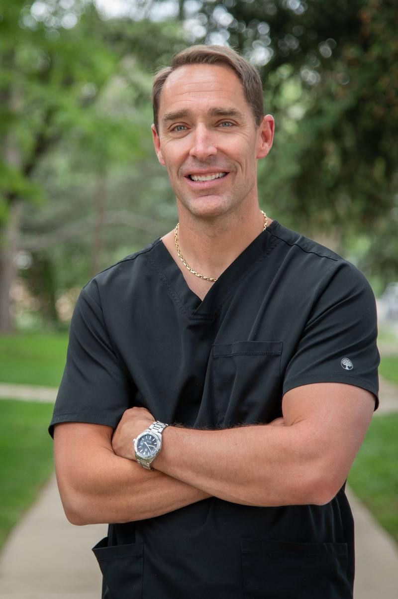 photo of Dr. Todd M. Roby, DDS, standing near a plant in the office